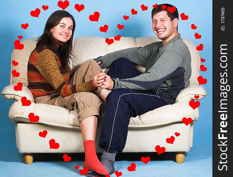 The young couple sitting on a sofa surrounded by rendered hearts