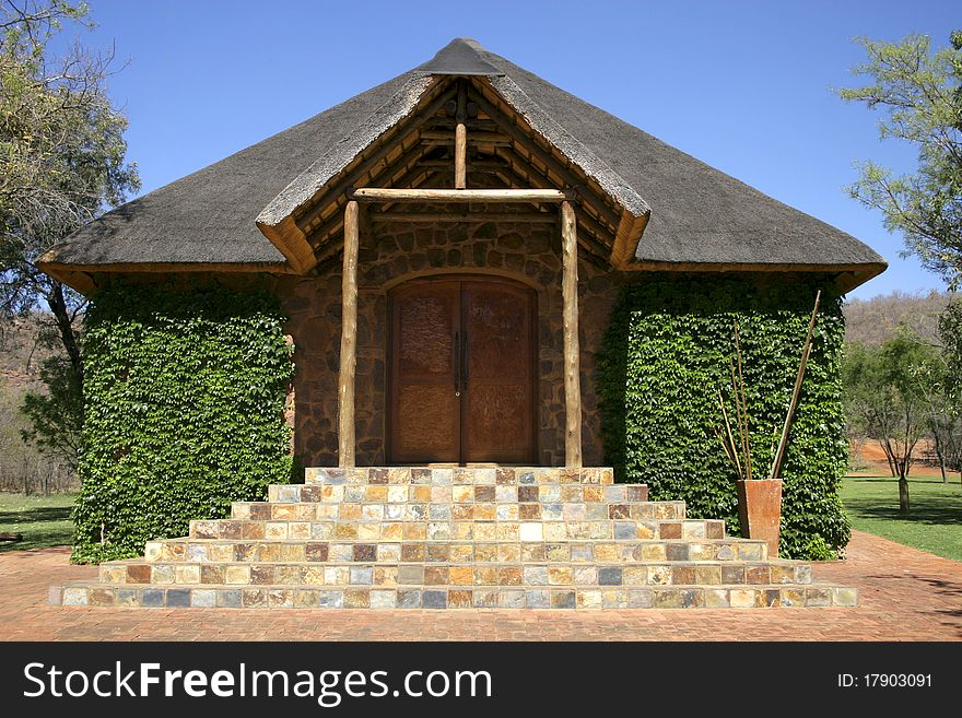 Stone chapel with thatch roof covered in green ivy against blue sky