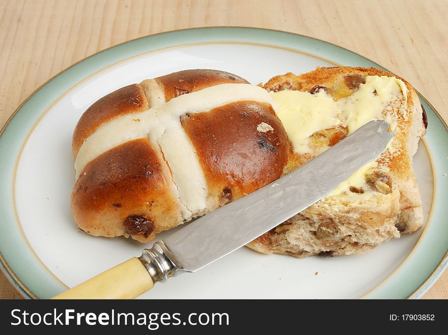 Toasted and buttered hot cross bun with a knife on a plate