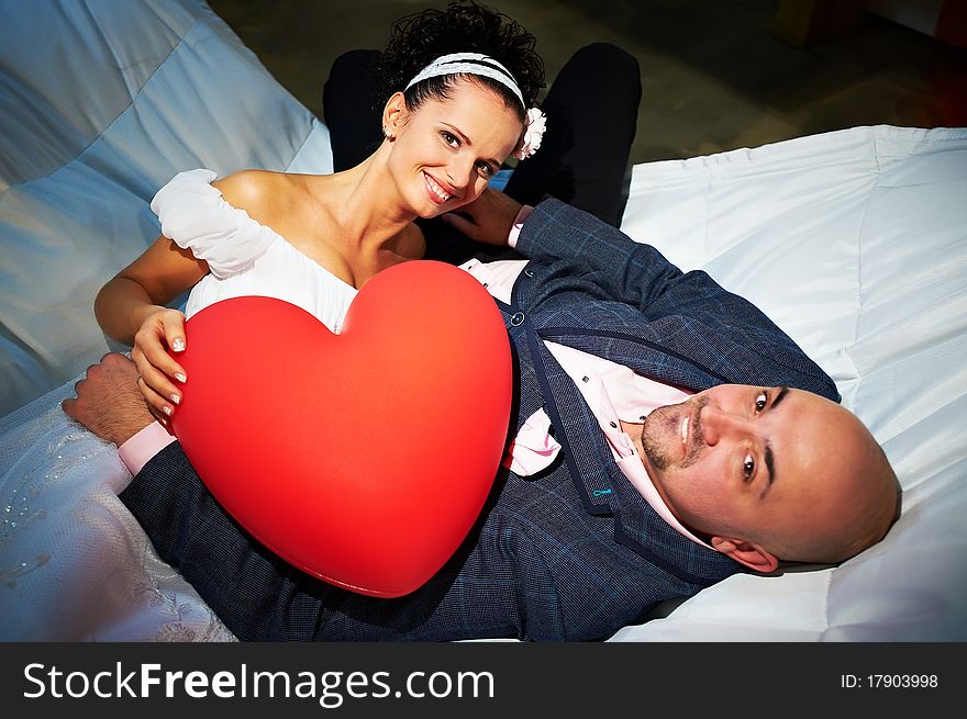 Joyful bride and groom with red toy heart