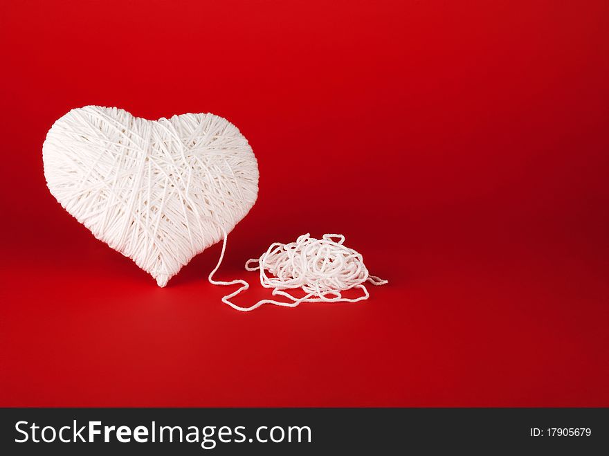 White heart made of wool on a red background.