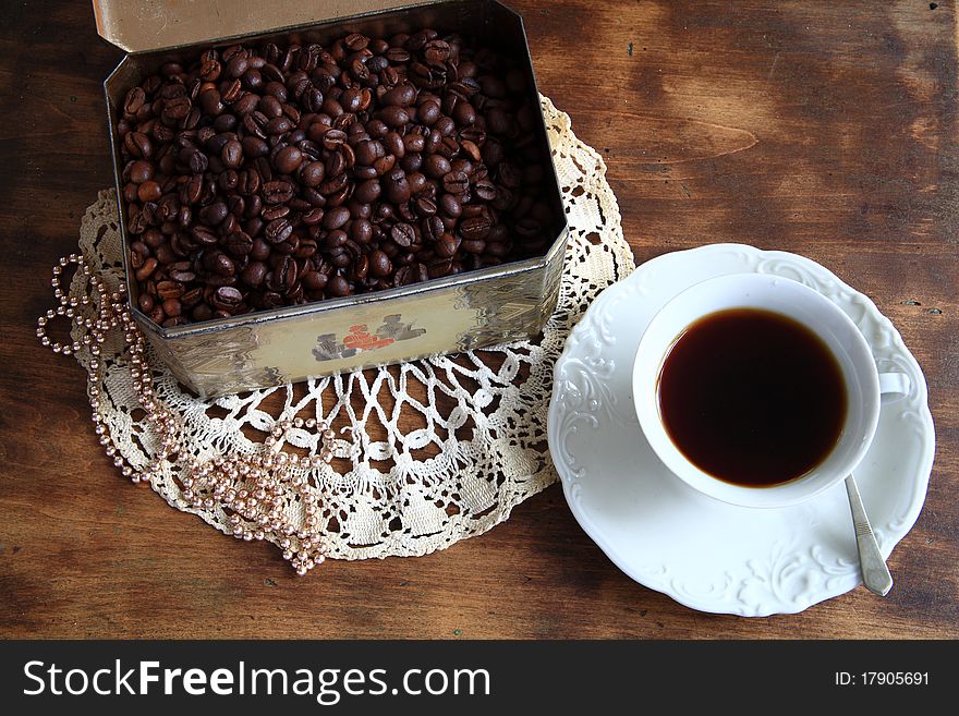 Coffee in white cup and box with roasted grain on wooden background.
