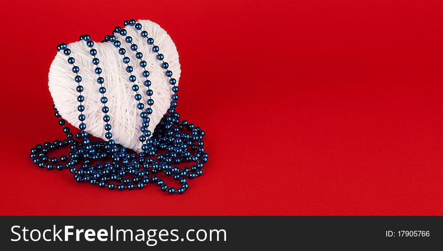 Beads on a white heart made of wool on a red background. Valentine's Day.