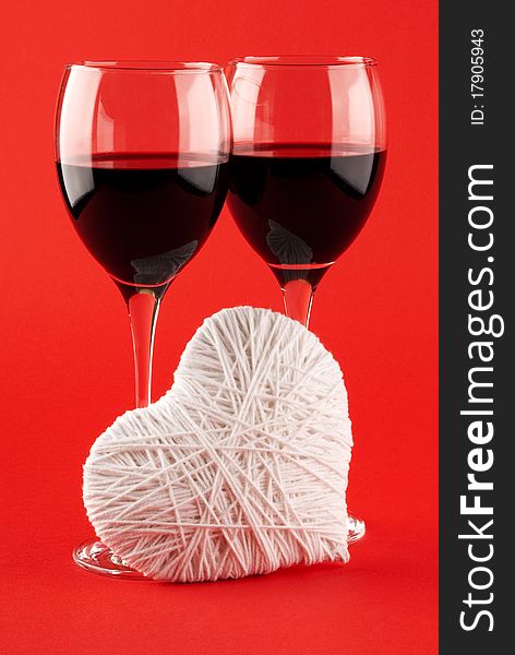 Two glasses of wine and a white heart made of wool