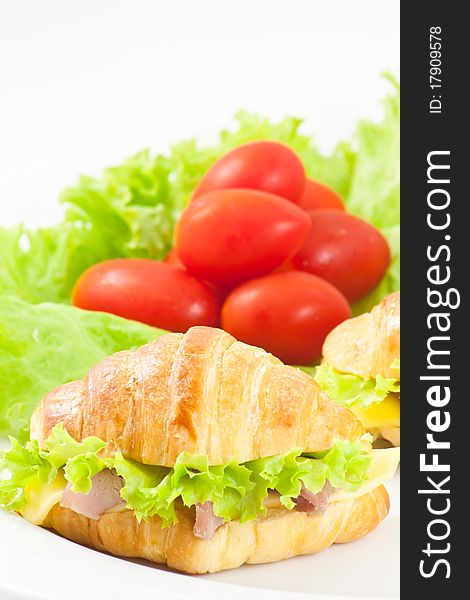 Ham and cheese croissant sandwich with tomato and lettuce in background