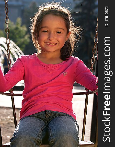 Portrait of smiling little girl on swing playground outdoors - looking at the camera