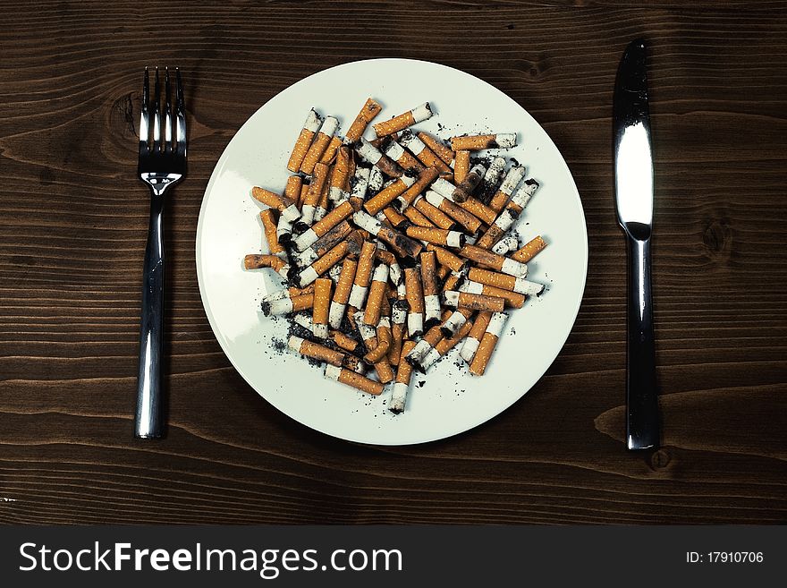 Plate with cigarettes stubs with cutlery on wood desk