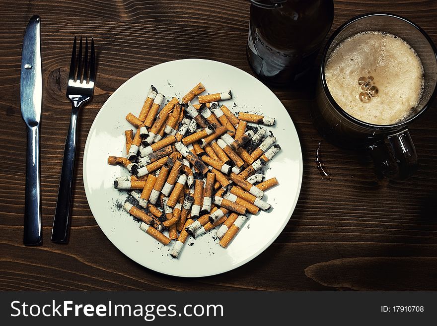 Plate with cigarettes stubs with fork and beer