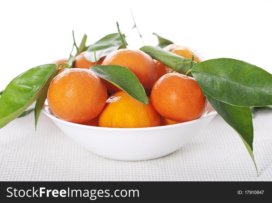 A bowl full of ripe tangerines with leaves
