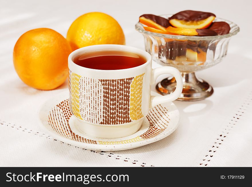 Tea drinking with delicious slices of orange coated chocolate and two oranges. Tea drinking with delicious slices of orange coated chocolate and two oranges