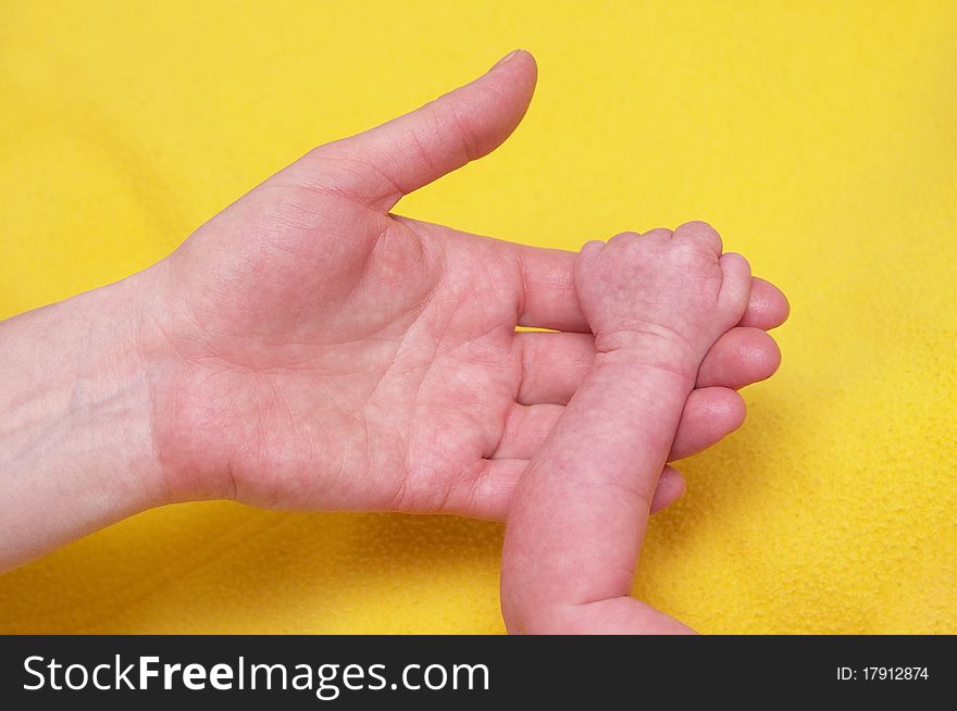 Newborn baby holding mother's hand over yellow towel. Newborn baby holding mother's hand over yellow towel