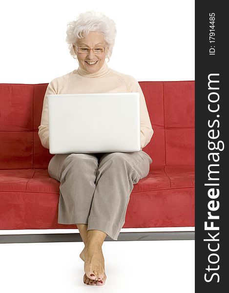 Elderly woman on the couch with laptop in a white background