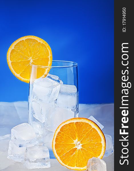 Empty Glass with orange slices stand on ice plate and it is surrounded by ice cubes.