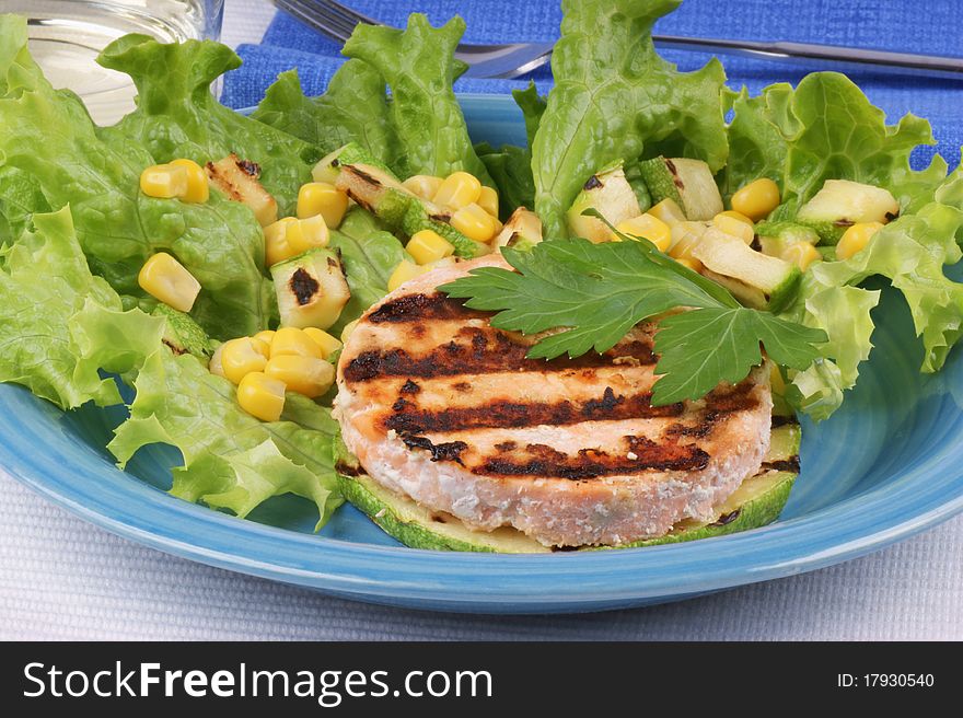 Grilled salmon and zucchini with salad and corn over a light blue plate. Studio shot