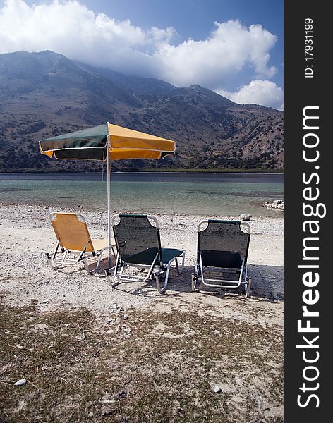 Three deck chairs and umbrellas on the background of the sea and mountains