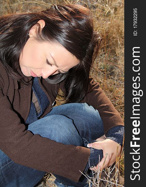 Beautiful brunette female sitting alone in a field. Beautiful brunette female sitting alone in a field