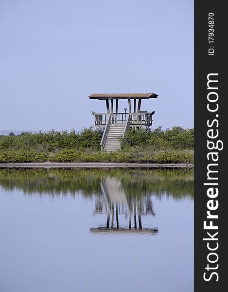 A wooden observation tower in a wildlife preserve is reflecting in the water with morning light. A wooden observation tower in a wildlife preserve is reflecting in the water with morning light.
