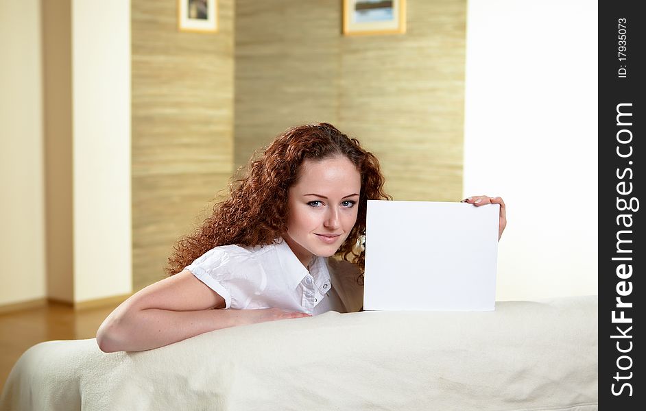 Young red hair woman sitting on a sofa and holding a white blank card. Young red hair woman sitting on a sofa and holding a white blank card