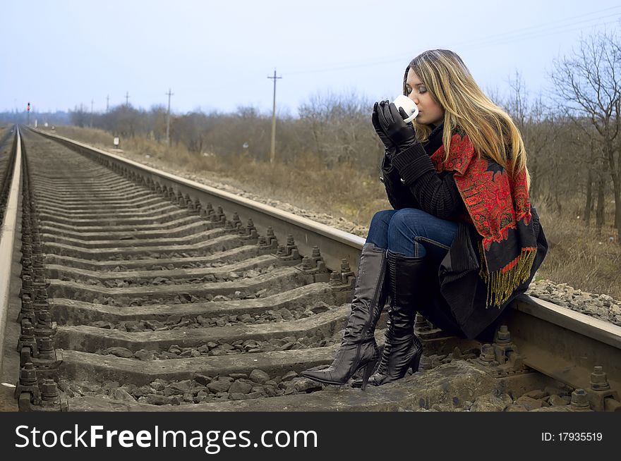 The girl sits on rails and drinks hot tea. The girl sits on rails and drinks hot tea