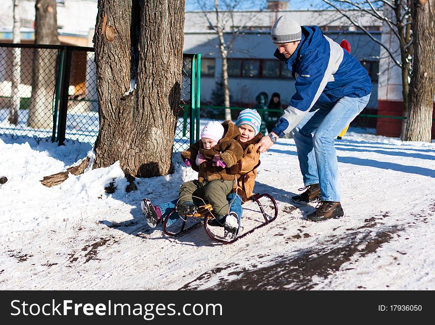 Father pushing children down the hill in a sled outdoor in winter
