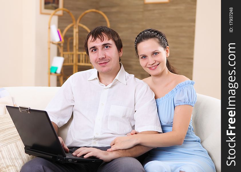 Young couple working on a laptop computer sitting on the sofa at home. Young couple working on a laptop computer sitting on the sofa at home