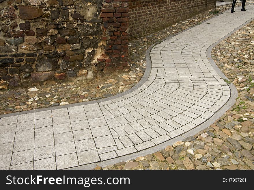 A modern grey path in an ancient surrounding of stones, someone is following the pathway. A modern grey path in an ancient surrounding of stones, someone is following the pathway