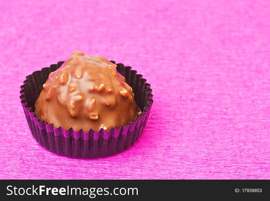 Milk chocolate sweet with hazelnut flakes on pink background