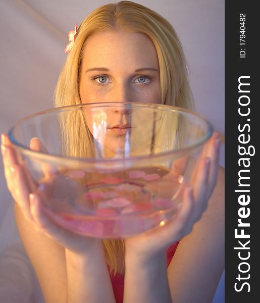 Young woman holding a glass bowl filled with water and pink petals. Young woman holding a glass bowl filled with water and pink petals