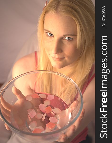 Young woman holding a glass bowl filled with water and pink petals. Young woman holding a glass bowl filled with water and pink petals