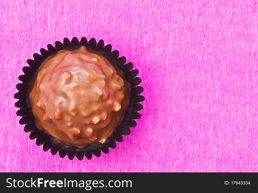 Milk chocolate sweet with hazelnut flakes on pink background