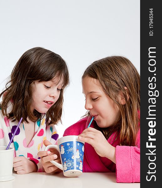 A couple of girls are enjoying sipping hot chocolate through straws. One is showing her cup to the other. A couple of girls are enjoying sipping hot chocolate through straws. One is showing her cup to the other.