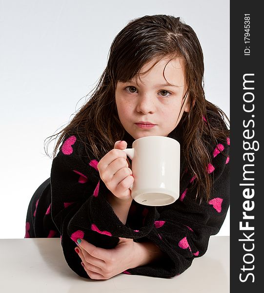 A girl in a robe sipping from a mug looks at the camera. A girl in a robe sipping from a mug looks at the camera