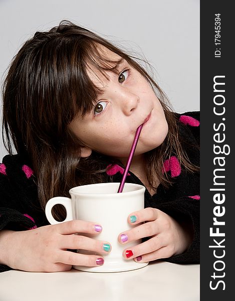 A girl enjoys sipping from a mug through a straw. A girl enjoys sipping from a mug through a straw