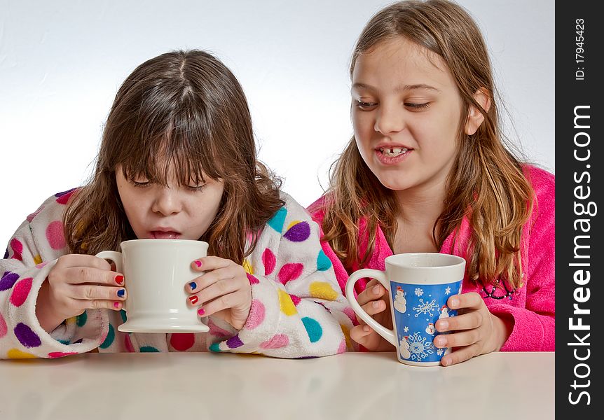 A girl looks on as one tastes her drink from a mug. A girl looks on as one tastes her drink from a mug.