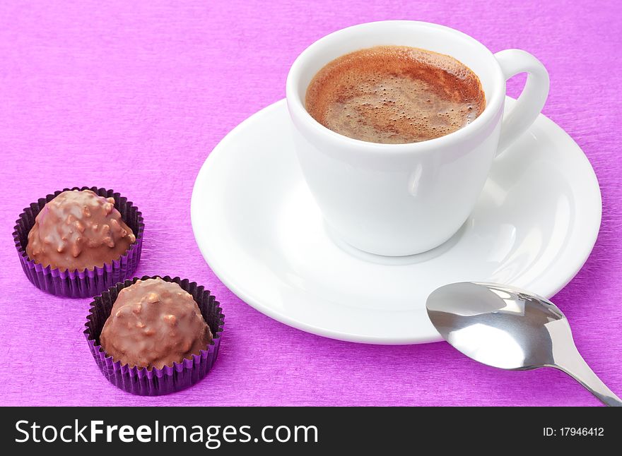 Freshly brewed hot coffee in white cup and milk chocolate sweets with hazelnut flakes on pink background. Freshly brewed hot coffee in white cup and milk chocolate sweets with hazelnut flakes on pink background