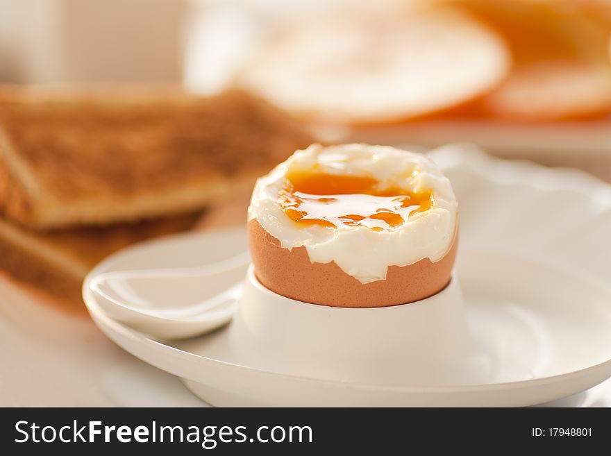 Soft boiled egg with toasted bread and slices of oranges in the back. Shallow depth of filed.