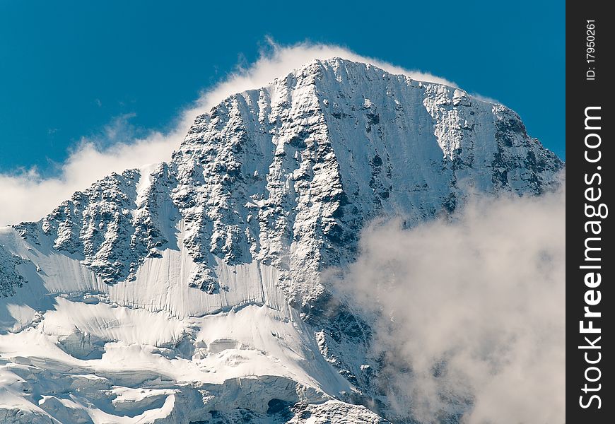 Snow-covered, rocky peak of Breithorn mountain in the Swiss Alps with a fringe of cloud and dramatic sidelighting set against a blue sky. Snow-covered, rocky peak of Breithorn mountain in the Swiss Alps with a fringe of cloud and dramatic sidelighting set against a blue sky