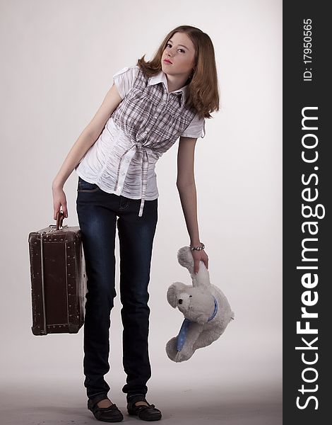 The girl is with a heavy suitcase and a toy on a gray background