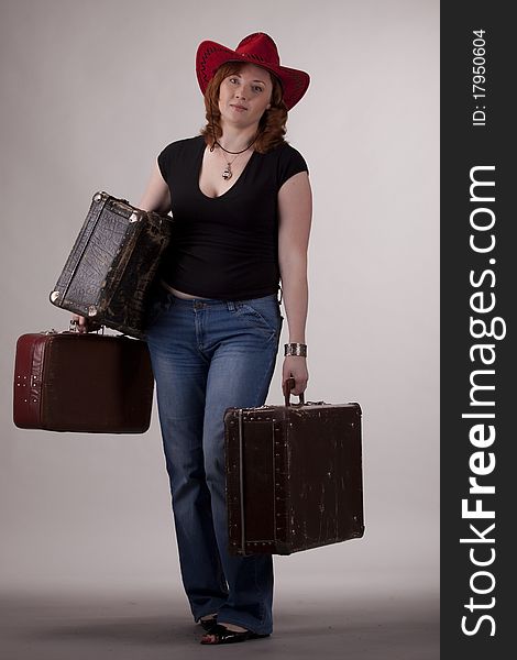 The girl in a red hat with old suitcases in hands on a gray background. The girl in a red hat with old suitcases in hands on a gray background