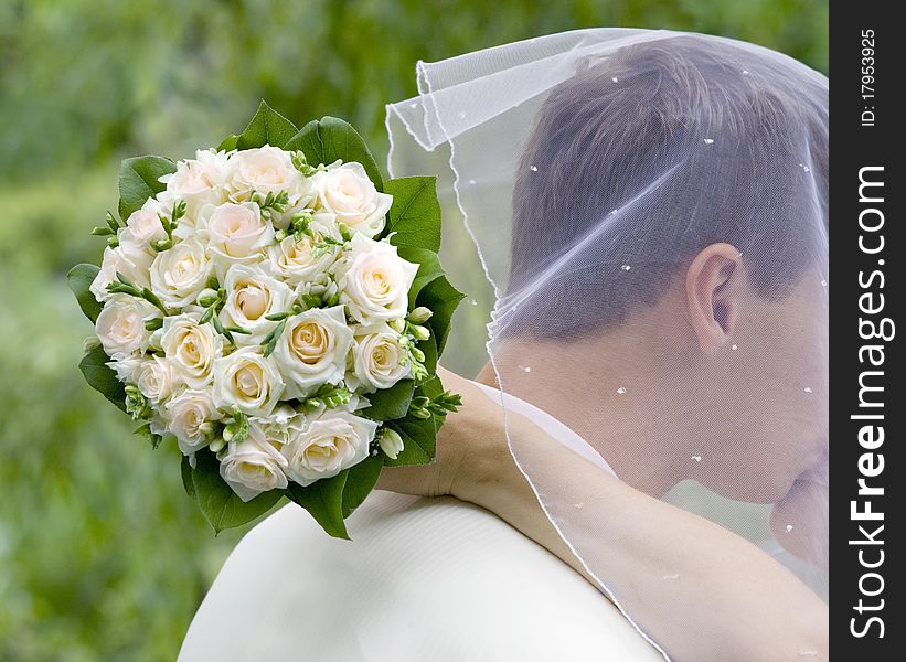 Bride kiss bridegroom, keeping flowers behing him. Bride kiss bridegroom, keeping flowers behing him