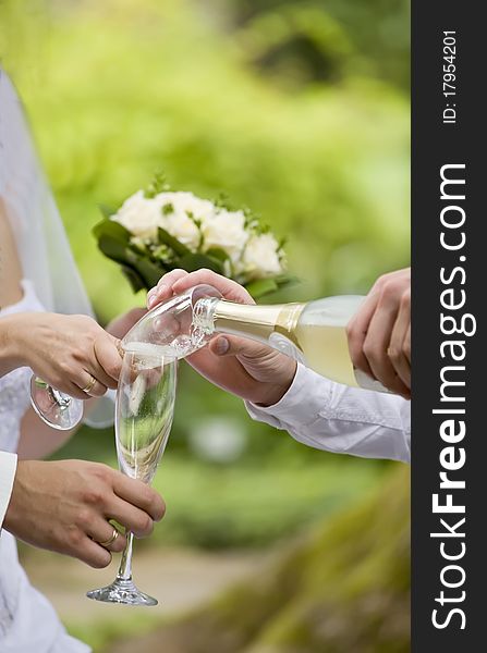 Somebody fills bride's and fiance's glasses with champagne