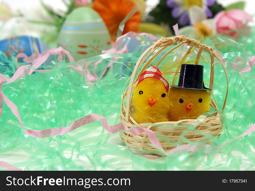 A couple of chicks in a basket with some eggs and flowers in the background. A couple of chicks in a basket with some eggs and flowers in the background.