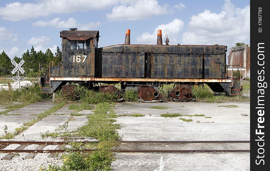 Old abandoned locomotive a by a rail crossing sign