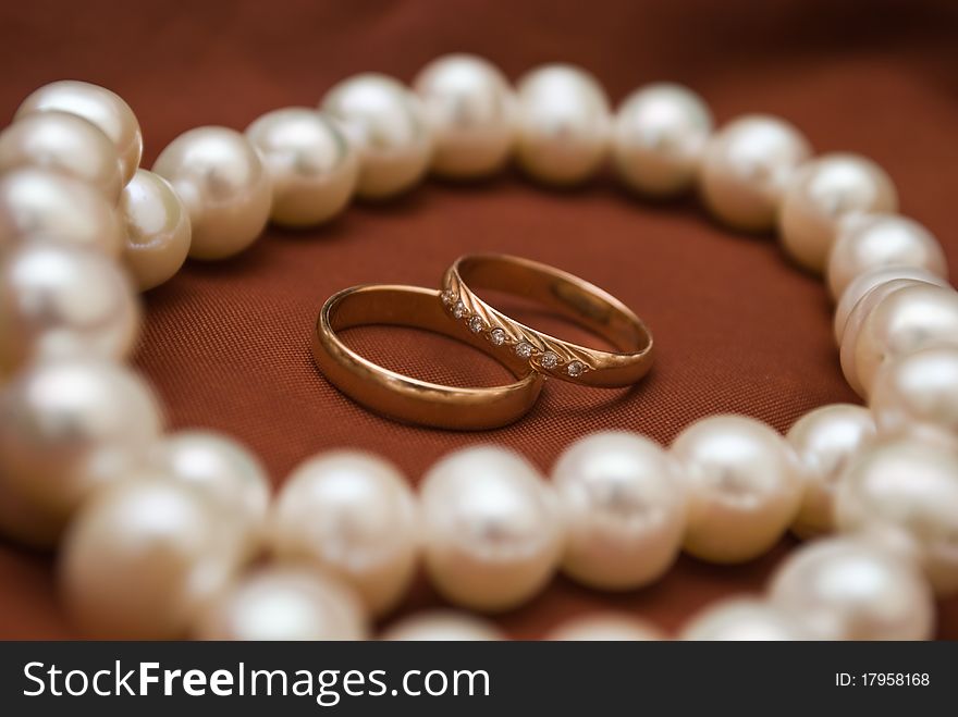 Weddings rings and white pearls on the coloured background. Weddings rings and white pearls on the coloured background