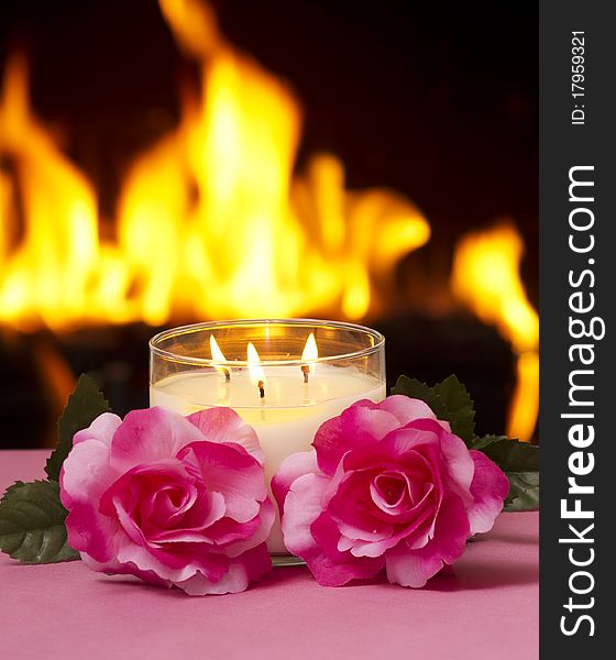 Two roses and a candle on a table with a fireplace in the background. Two roses and a candle on a table with a fireplace in the background.