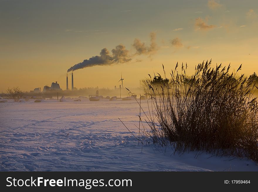 Sunrise in the beautiful misty snowy landscape. In the background is a great plant and windmills for alternative energy