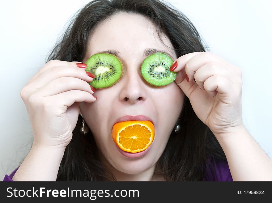 Woman holds two slices of kiwi before her eyes and orange fruit in mouth