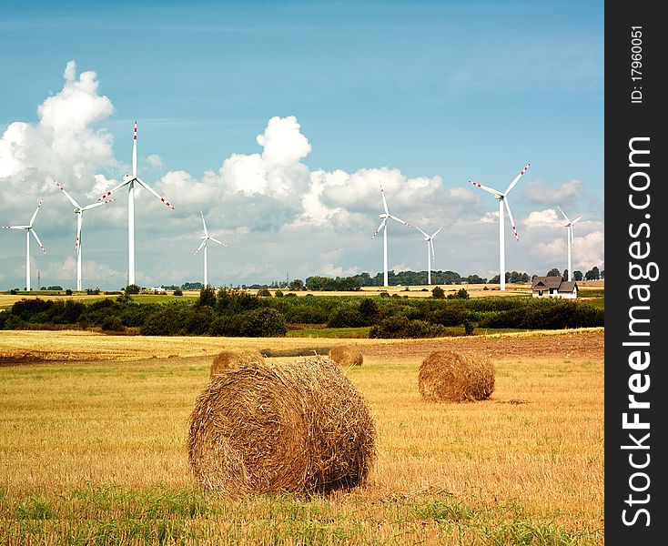 Windturbines and summer harvest field with haybales. Windturbines and summer harvest field with haybales