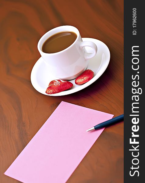 Coffee cup on the table with chocolates, a pink card and a pen. Coffee cup on the table with chocolates, a pink card and a pen.