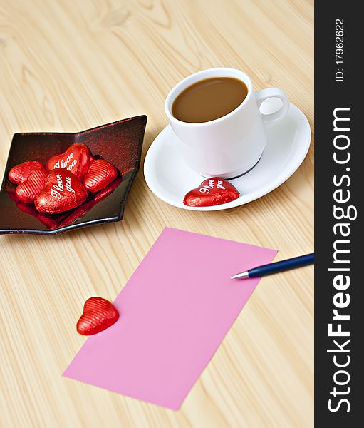 Coffee cup on the table with chocolates, a pink card and a pen. Coffee cup on the table with chocolates, a pink card and a pen.